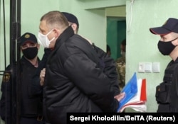 A handcuffed Syarhey Tsikhanouski is shown being escorted into the defendants' cage during his December 14, 2021 court sentencing.