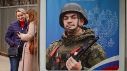 Женщины на автобусной остановке в Москве рядом с объявлением о призыве в армию, на котором изображен российский солдат, 8 апреля 2024 года, фото EPA-EFE
