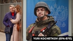Женщины на автобусной остановке в Москве рядом с объявлением о призыве в армию, на котором изображен российский солдат, 8 апреля 2024 года, фото EPA-EFE