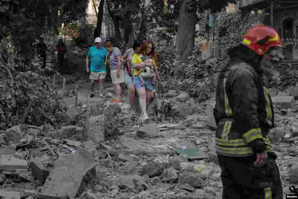 Местные жители идут по обломкам жилого дома, разрушенного во время российских ракетных ударов