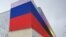 RUSSIA -- A communal worker clears snow in front of a huge advertising screen displaying the Russian national tricolor flag in Moscow on January 16, 2024. 