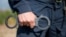 Detail of a police officer holding handcuffs. Selective focus with shallow depth of field.