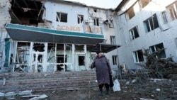Женщина стоит у разрушенной больницы в захваченной российскими войсками Волновахе