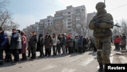 Российский военный и жители осажденного и заблокированного Мариуполя в очереди за гуманитарной помощью. 23 марта 2022 года. Фото: Reuters