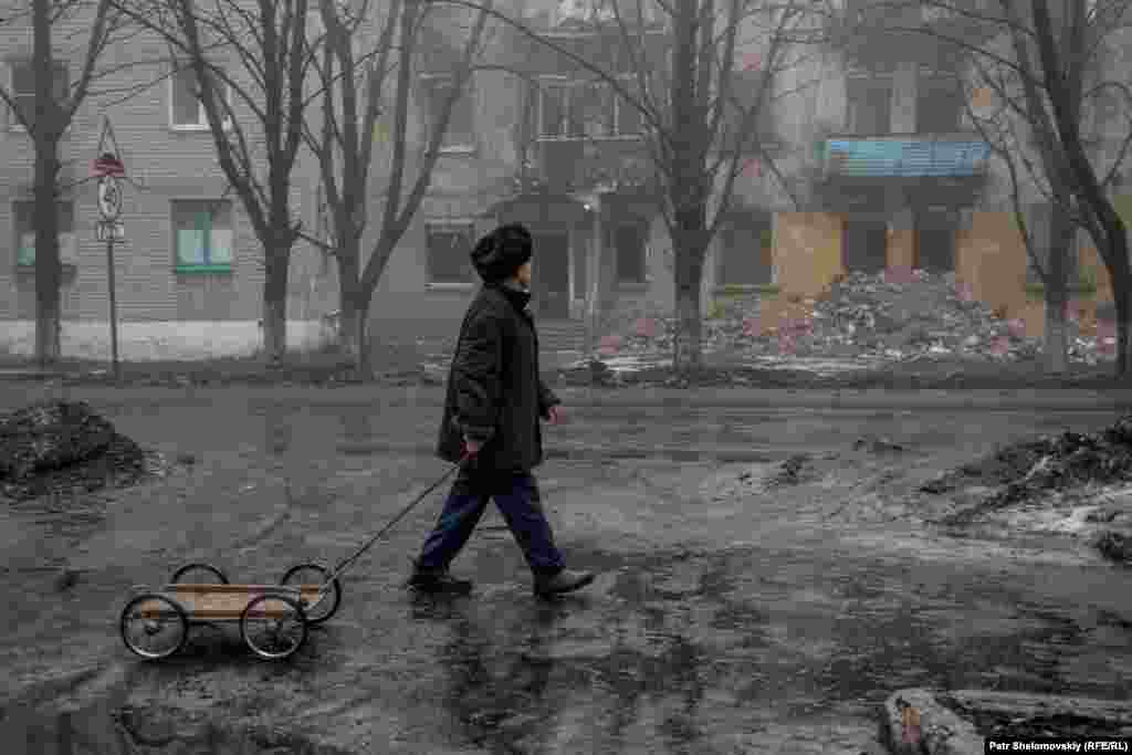 Мужчина с тележкой проходит мимо разрушенного здания