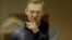 RUSSIA -- Russian opposition leader Aleksei Navalny, charged with defaming a World War II veteran, gestures from inside a glass cell during a court hearing in Moscow, February 16, 2021