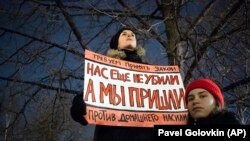 In November 2019, a woman in Moscow holds a banner that demands Russia adopt a law against domestic violence. "They haven't killed us yet," the poster reads. 