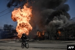 Велосипедист проезжает мимо горящих после обстрела Харькова зданий, 25 марта 2022 года. Фото: AFP