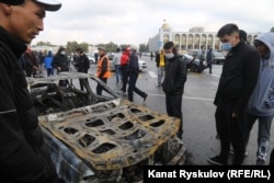 Pedestrians observe a car damaged during the clashes of October 5-6, 2020 in Bishkek that left some 686 people injured.
