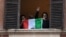 Italy -- Men gesture holding an Italian flag as they look out of an apartment window as part of a flashmob organised to raise morale during Italy's coronavirus crisis in Rome, Italy, March 13, 2020. REUTERS/Alberto Lingria