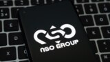 NSO Group logo seen on the smartphone placed on laptop keyboard. Israeli company known for its Pegasus spyware for surveillance.