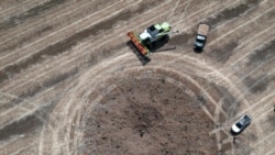 Украинский фермер собирает урожай в поле, куда упала российская ракета и оставила воронку 4 июля 2022 года