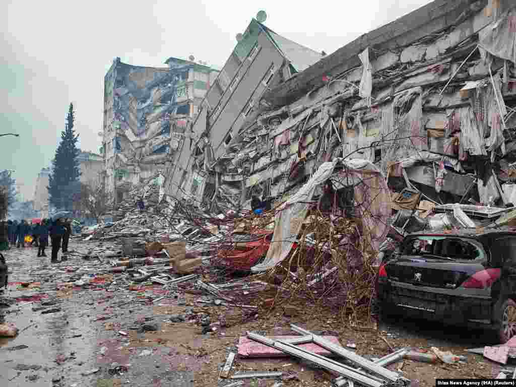 Люди стоят перед разрушенными зданиями после землетрясения в турецком Кахраманмарасе