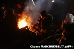 Migrants warm themselves by a fire in a camp on the Belarusian-Polish border in Belarus' Hrodno region on November 14, 2021.