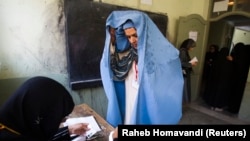 Афганская женщина показывает свое лицо сотруднице избирательной комиссии во время выборов. 18 сентября 2010 года