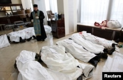 A priest stands in the lobby of the Hotel Ukraine, surrounded by the bodies of Euromaidan protesters killed during clashes with riot police in Kyiv on February 20, 2014.