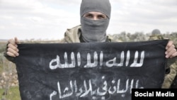 Член "Исламского государства", известный как "Абдулла Таджик", держит в руках флаг, на котором написано "Талибан в земле Леванта" 