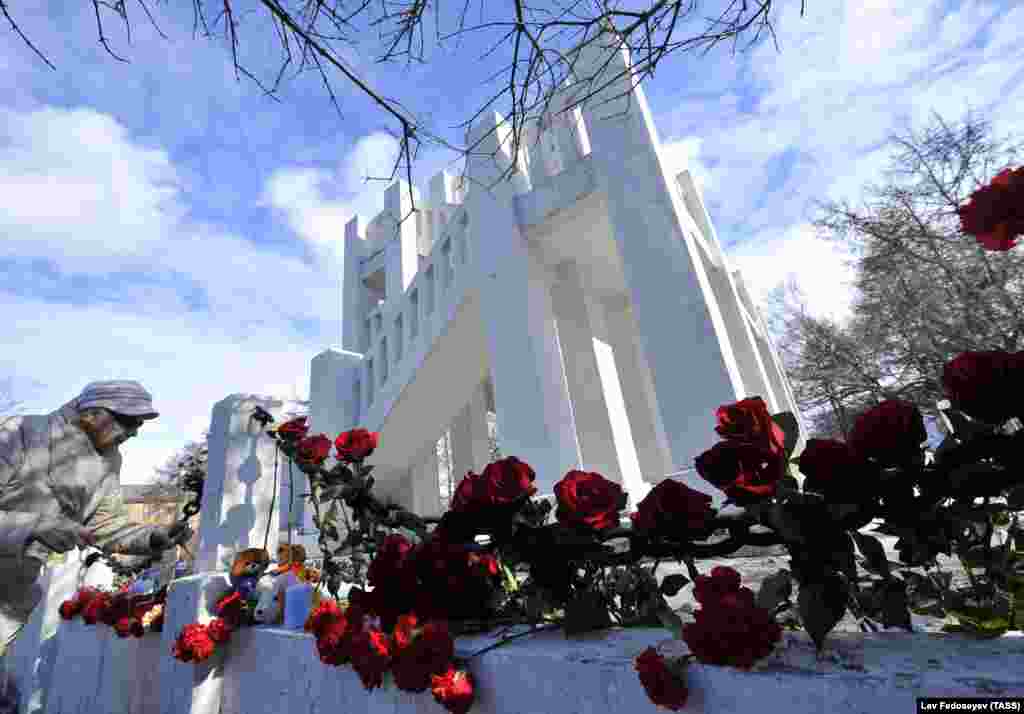 Женщина кладет цветы к стихийному мемориалу у памятника жертвам интервенции в Мурманске &ndash; в память о погибших в аварии