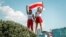 Two women display a former Belarusian national flag, a symbol of opposition to the government,  during a Minsk rally on August 16, 2020 against police violence and Belarus' official presidential election results.