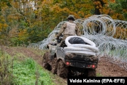 A Latvian soldier patrols along a new barbed wire fence, donated by Slovenia, erected on September 28, 2021 on Latvia's border with Belarus.
