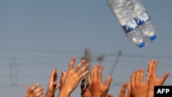 Волонтеры кидают мигрантам воду, пока те ждут на границе между Грецией и Македонией