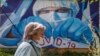 RUSSIA -- A woman wearing protective mask walks in front of a coronavirus graffiti showing a doctor with a face mask strangling with the coronavirus disease (COVID-19) pandemic on a wall in front of hospital in Krasnogorsk, Moscow region, May 15, 2020