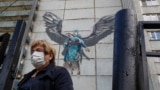 RUSSIA HEALTH CORONAVIRUS COVID19 -- A woman wearing protective mask walks in front of a coronavirus graffiti showing a doctor with a face mask tries to help a patient with the coronavirus disease (COVID-19) on a wall of a multi-storey residential buildi