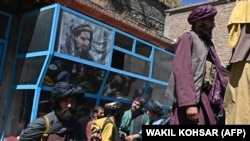 Taliban fighters stand beneath an image of legendary slain resistance fighter Ahmad Shah Masud in the Panjshir region's Bazark district on September 15, 2021, days after the hardline Islamist group announced the capture of the last province resisting their rule.