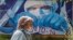 RUSSIA -- A woman wearing protective mask walks in front of a coronavirus graffiti showing a doctor with a face mask strangling with the coronavirus disease (COVID-19) pandemic on a wall in front of hospital in Krasnogorsk, Moscow region, May 15, 2020