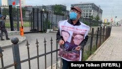 Житель Алматы Женис Заркын с плакатом с фото своих родственников приковал себя к ограде у посольства Китая