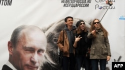 Молодые люди делают селфи на фоне баннера с президентом России Владимиром Путиным. Санкт-Петербург, 2 мая 2015