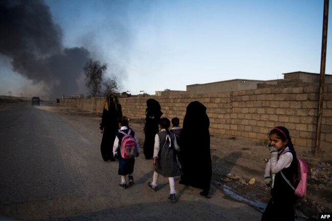 Жительницы освобожденного Мосула идут вдоль дороги. Перед выходом из Мосула члены ИГИЛ поджигали нефтяные разливы, чтобы затруднить операцию коалиции по освобождению