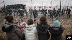 Migrant children stand in front of a barbed wire fence and Polish servicemen on the Belarusian side of Poland's Kuznitsa checkpoint on November 17, 2021, as reports first surfaced of the migrants' withdrawal from the area, under Belarusian forces' supervision. 
