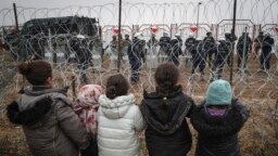 Migrant children stand in front of a barbed wire fence and Polish servicemen on the Belarusian side of Poland's Kuznitsa checkpoint on November 17, 2021, as reports first surfaced of the migrants' withdrawal from the area, under Belarusian forces' supervision. 