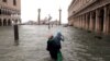 Italy -- A woman holds a child as she walks in a flooded Saint Mark Square during a period of seasonal high water in Venice, Italy October 29, 2018 