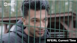 Iranian migrant Amir Chani speaks with Current Time through the fence surrounding Latvia's Mucenieki detention center for illegal migrants. A recent outbreak of COVID-19 cases led to all of the center's 262 residents being placed under quarantine. 