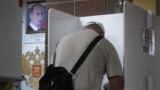 RUSSIA -- A man wearing a protective face mask and gloves prepares to cast his ballot during early voting in a referendum on amendments to the Russian Constitution next to a portrait of Russian President Vladimir Putin at a polling station in Moscow, June