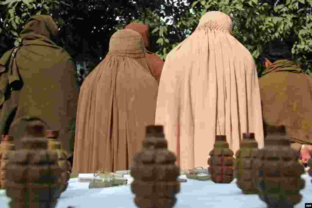 Бывшие боевики Талибана, включая двух женщин, в полицейском участке на фоне изъятого в результате военной операции в провинции Нангархар (Nangarhar) Афганистана оружия и боеприпасов. 4 февраля. (Abdul Mueed, epa)