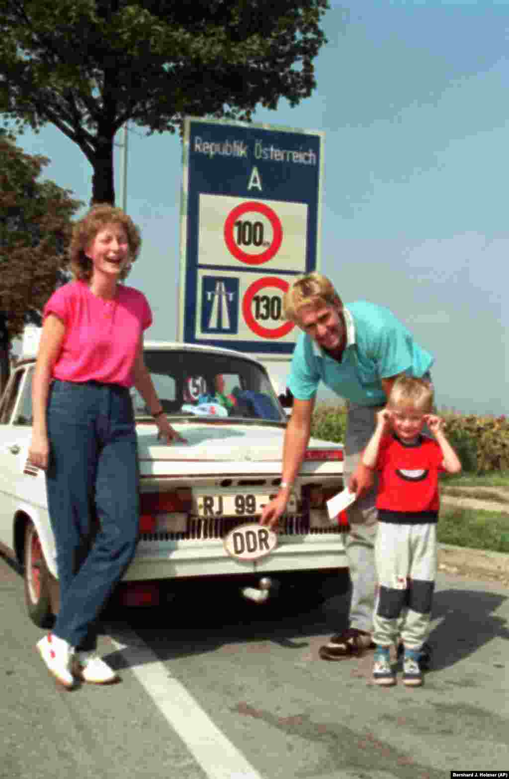Семья из Восточной Германии снимает знак DDR (Deutsche Demokratische Republik &ndash; Германская Демократическая Республика) после въезда в Клингенбах в Австрии