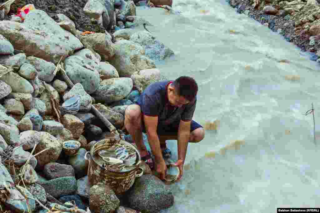 На фото - мужчина моет в реке посуду, на которой после селя осталась глина