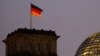 A German national flag flies atop the illuminated Reichstag building in Berlin
