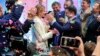 UKRAINE -- Ukrainian comedian and presidential candidate Volodymyr Zelenskiy, center right, and his wife Olena Zelenska, center left, greet their supporters at his headquarters as the portrait of Ukrainian President Petro Poroshenko is seen on a TV screen