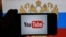 RUSSIA  -- A hand holding a smartphone with the logo of the Youtube video sharing website on the screen, in front of a computer screen showing a Russian national flag and coat of arms, St. Petersburg, December 2, 2016