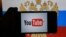 RUSSIA  -- A hand holding a smartphone with the logo of the Youtube video sharing website on the screen, in front of a computer screen showing a Russian national flag and coat of arms, St. Petersburg, December 2, 2016