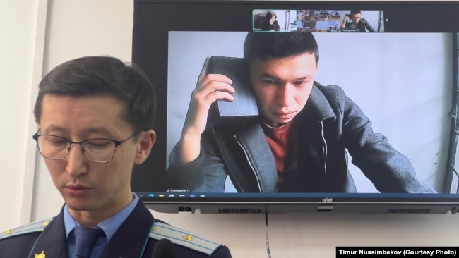 Темирлан Енсебек, автор Qaznews24 (на экране) и прокурор Дидар Кабаев (на переднем фоне). 9 апреля 2025 года