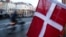 A cyclist passes a Danish flag in the Nyhavn area at sunset in Copenhagen