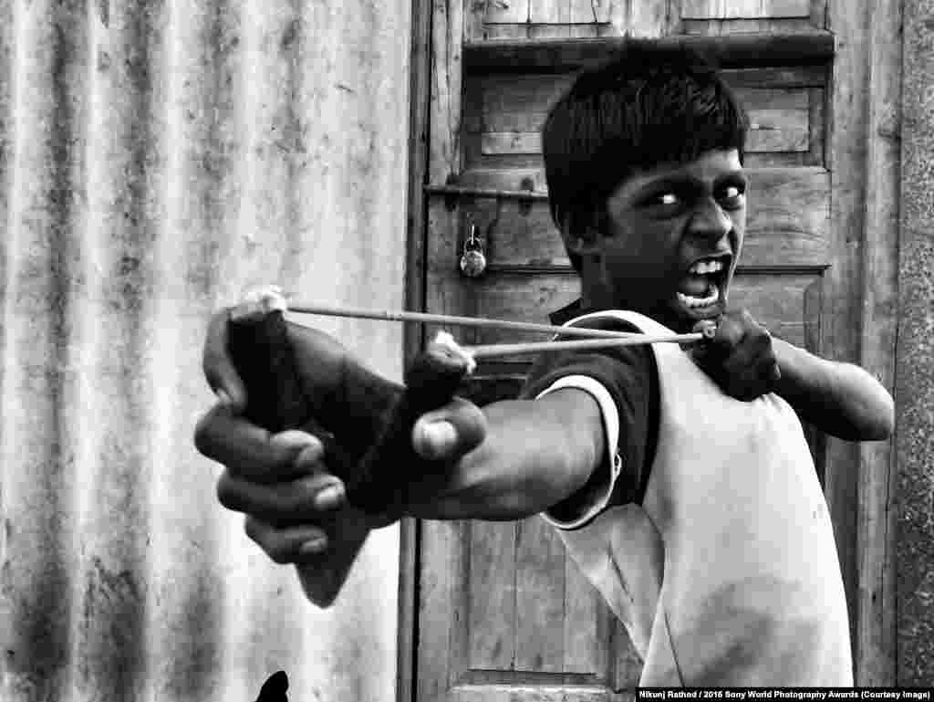 Мальчик на фото стрелял из рогатки по птицам со своими друзьями в одном из заброшеных районов Мумбая. После того, как фотограф попросил ребят продемострировать их мастерство на камеру, ребята устроили настоящее соревнование