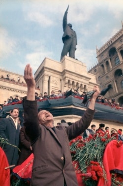 An unidentified man lifts his arms in grief under a statue of Lenin during a mass funeral in Baku on January 27, 1990.