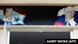 Портреты свергнутого президента Сирии Башара Асада и главы России Владимира Путина над входом в здание, которое использовалось российской армией в сирийском городе Аль-Басса в провинции Латакия, 12 декабря 2024 г. Фото AFP