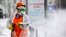 RUSSIA -- A municipal worker, wearing special suit to protect against coronavirus, sprays disinfectant as a precaution against the coronavirus, on an empty street with a billboard reads "Stay home, take care of yourself and your loved ones" in Moscow, Rus